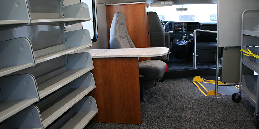 empty shelves next to an empty counter with a seat behind it. 
